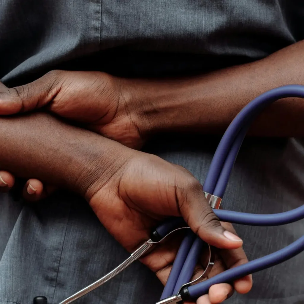 Medical professional in gray scrubs holding stethoscope behind back.